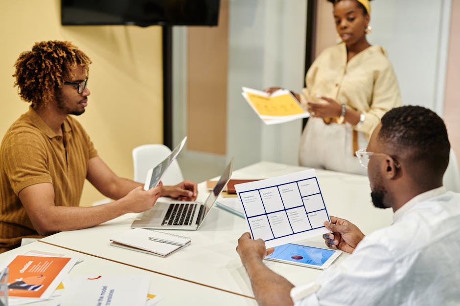 Group of coworkers collaborating in a modern office environment with laptops and documents.